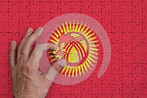 Kyrgyzstan flag is depicted on a puzzle, which the man`s hand completes to fold