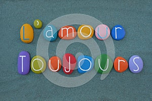 L`amour toujours, french phrase meaning Love always composed with handmade multicolored stone letters over green sand photo