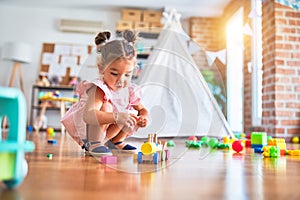 l toddler sitting on the floor playing with wooden train toy at kindergaten