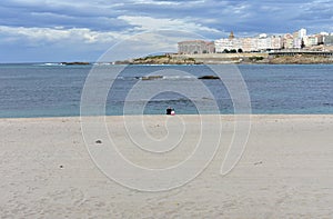 Riazor Beach with old man and little girl sitting on the sand. Sunset, rainy day, La Coruna, Spain. photo