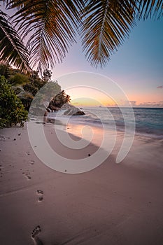 La Digue Island, Seychelles. Beautiful sunset lit colorful sky on exotic tropical sandy beach with foot prints