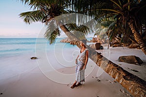 La Digue, Seychelles. A woman near coconut palm tree in a gold sunset light on a tropical beautiful sandy beach