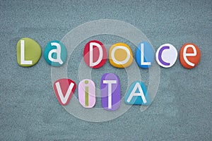 La dolce vita, italian lifestyle slogan composed with multi colored stone letters over green sand