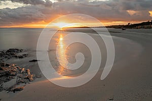 La Pelosa beach in Sardinia at sunrise with a sunburst and rocks in the foreground