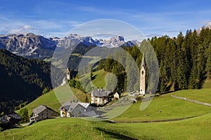 La Vale - Italian Dolomites, a small village in the mountains, right by a high forest stands a slender church, on the left on the