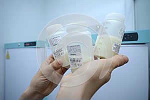 Lab assistant hand holding breast milk storage containers with human milk, freezers on a background. Human Milk Bank laboratory