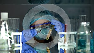 Lab assistant studying meat sample with magnifying glass, helminth analysis