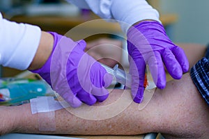 Lab tech in purple gloves taking blood from patient