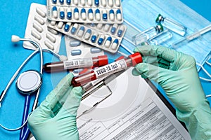 Lab technician assistant or doctor wearing rubber or latex gloves holding blood test tube over clipboard with blank form