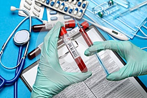 Lab technician assistant or doctor wearing rubber or latex gloves holding blood test tube over clipboard with blank form