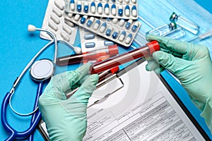 Lab technician assistant or doctor wearing rubber or latex gloves holding blood test tube over clipboard with blank form
