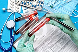 Lab technician assistant or doctor wearing rubber or latex gloves holding blood test tube over clipboard with blank form