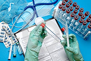 Lab technician assistant or doctor wearing rubber or latex gloves holding blood test tube and syringe over clipboard