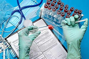 Lab technician assistant or doctor wearing rubber or latex gloves holding blood test tube and syringe over clipboard