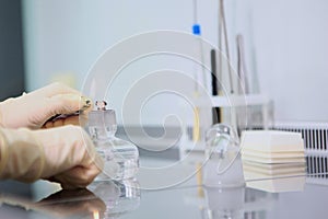 The lab technician lights an alcohol burner with a lighter. The hand of the laboratory assistant in protective gloves.The concept