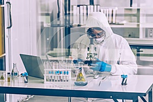 Lab Technician in Personal protective equipment  PPE suit looking into microscopes glass windows on foreground