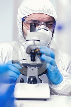 Lab technician in ppe analysing sample on microscope