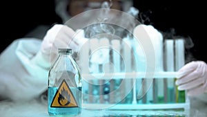 Lab worker analyzing evaporating liquid in tube, bottle with flame sign near