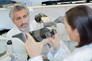 Lab worker holding microscope and talking to colleague photo