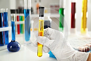 Lab worker holding test tube with yellow liquid near table