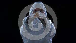 Lab worker in protective suit showing flame caution sign against dark background