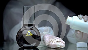 Lab worker showing pills, toxic liquid in flask on table, antidote development photo