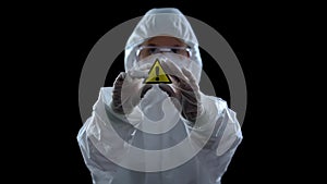 Lab worker in suit holding generic caution symbol in hands, black background