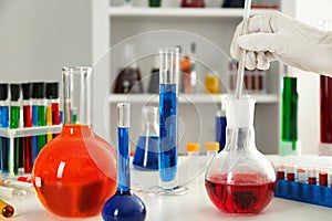 Lab worker taking sample of red liquid from flask on table