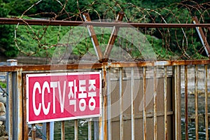 Label of CCTV operating on the rusty metal door in the restricted area in South Korea. The Korean language means