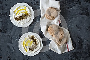 Labneh labaneh middle eastern soft white goat`s milk cheese with olive oil ,olives , za`atar , lemon, with pita bread over blac