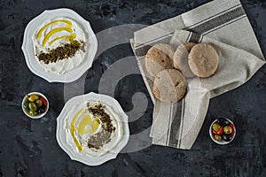 Labneh labaneh middle eastern soft white goat`s milk cheese with olive oil ,olives , za`atar , lemon, with pita bread over blac