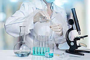 A laboratory assistant is making some experiments with a microscope and substances in test tubes and flasks