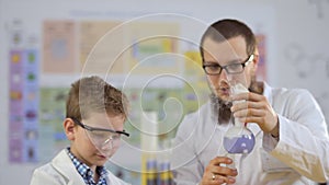 Laboratory assistant with pupil looks at steaming colorful liquids in flasks