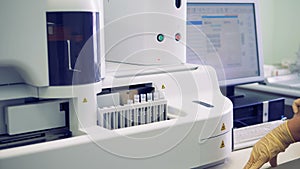 Laboratory assistant is setting readings on the computer and test tubes are installed into a machine