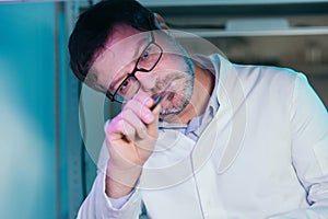 A laboratory assistant's hand holds a corn seed in tweezers, and corn seeds in a petri dish are decorated with