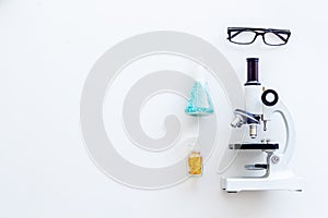 Laboratory desk with glasses, pills in test tube and microscope on white background top view space for text