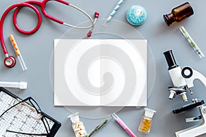 Laboratory desk with notebook, stethoscope, test tube and microscope on gray background top view space for text