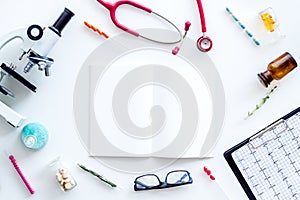 Laboratory desk with notebook, stethoscope, test tube and microscope on white background top view space for text