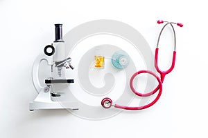 Laboratory desk with stethoscope, pills in test tube and microscope on white background top view