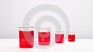 Laboratory equipment, beakers filled by red liquid on white table. Science concept.