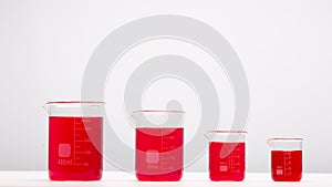 Laboratory equipment, beakers filled by red liquid on white table. Science concept.