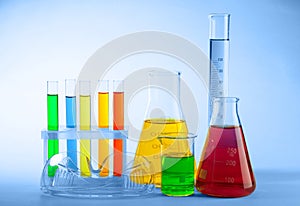 Laboratory glassware with colorful liquids and protective glasses on light background