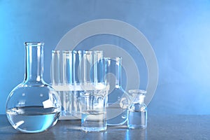 Laboratory glassware with liquid samples for analysis on table against toned blue background