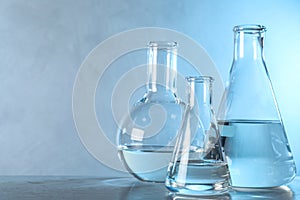 Laboratory glassware with liquid samples for analysis on table against toned blue background