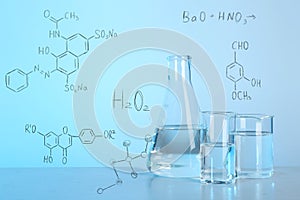 Laboratory glassware with liquids for analysis on table and chemical formulas