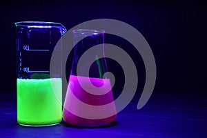 Laboratory glassware with luminous liquids on table against dark background, space for text