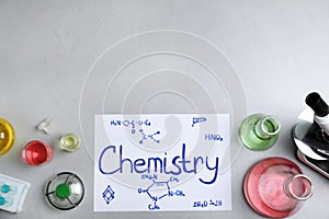 Laboratory glassware and paper with word CHEMISTRY on grey background, top view