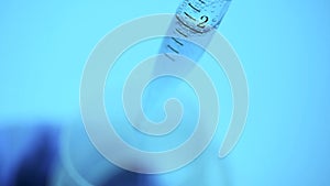 In the laboratory, a scientist with a pipette analyzes a colored liquid of blue color from a test tube.