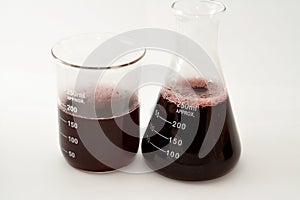 A laboratory set of glassware of conical and volumetric flasks that contains dark red liquid fluid with bubbles after a scientific