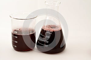 A laboratory set of glassware of conical and volumetric flasks that contains dark red liquid fluid with bubbles after a scientific